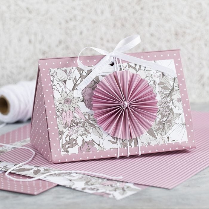 Geschenkverpackung in Rosa, verziert mit Rosette und Designpapier