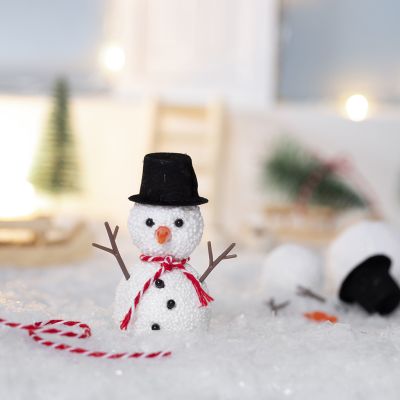 Der kleine Kobold baut einen Schneemann vor seinem Haus