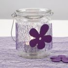 Ein Teelichthalter aus Glas, verziert mit lilafarbener Bordüre aus Netzgewebe und Filzblume